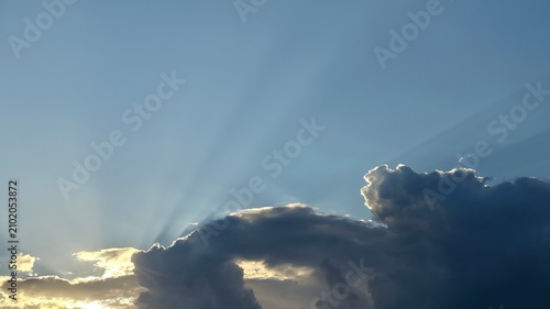 Foto Sunlight rays piercing through dark clouds in blue sky