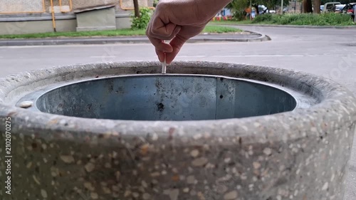Man drops a cigarette butt into a concrete trash can on an outdoor city street. smoking habits, throwing garbage, city litter bin, urban pollution.