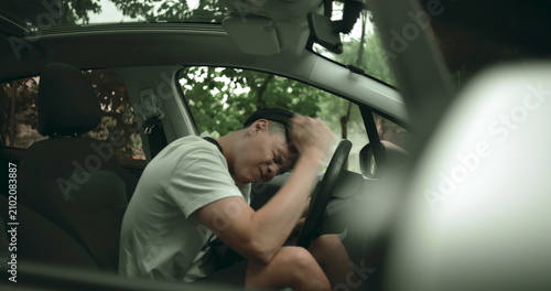 Принти на полотні Man sitting in driver seat with hand covering face, expressing frustration and m
