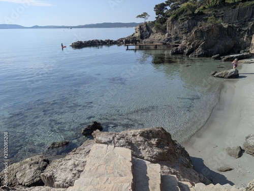 Εκτύπωση καμβά Small sandy cove with clear waters, stone steps, and bathers on the French Riviera, Giens, France