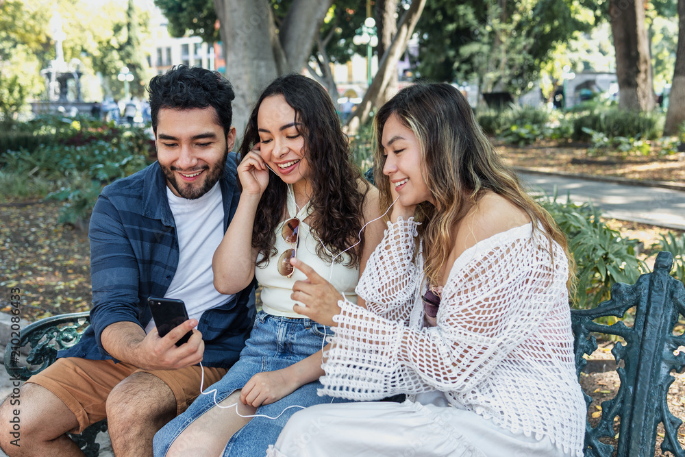 Fototapeta premium group of latin friends listening music and using headphones and having fun in public park in Mexico Latin America