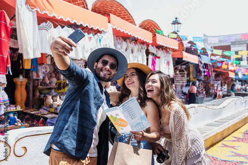 young latinos friends travellers taking a photo selfie in tourist market in Mexico Latin America, hispanic backpackers people in vacations