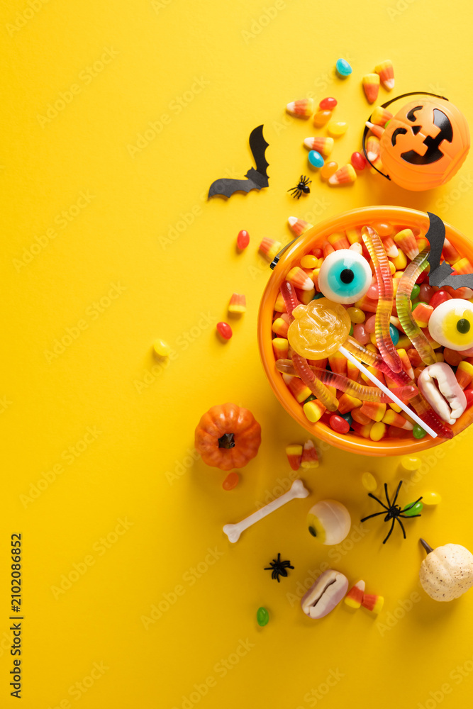 Fototapeta premium Happy Halloween vertical bowl of candy with pumpkin bucket, gummy worms, eyeball sweets and spooky decorations