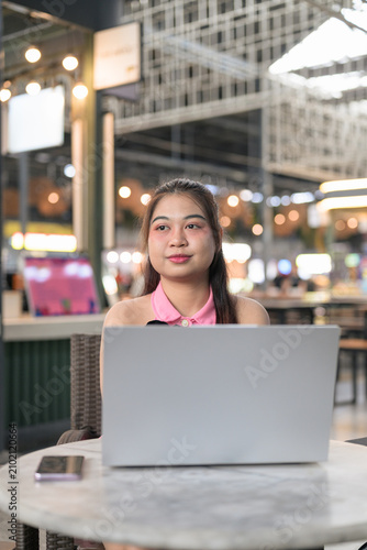 Relaxed Thai Isan woman taking a break behind her laptop at a food hall