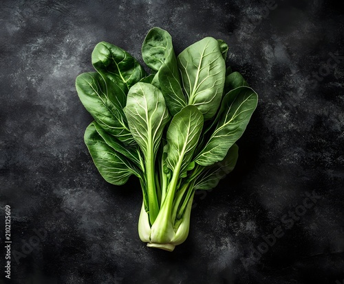 Fresh bok choy with water droplets on dark textured background overhead.