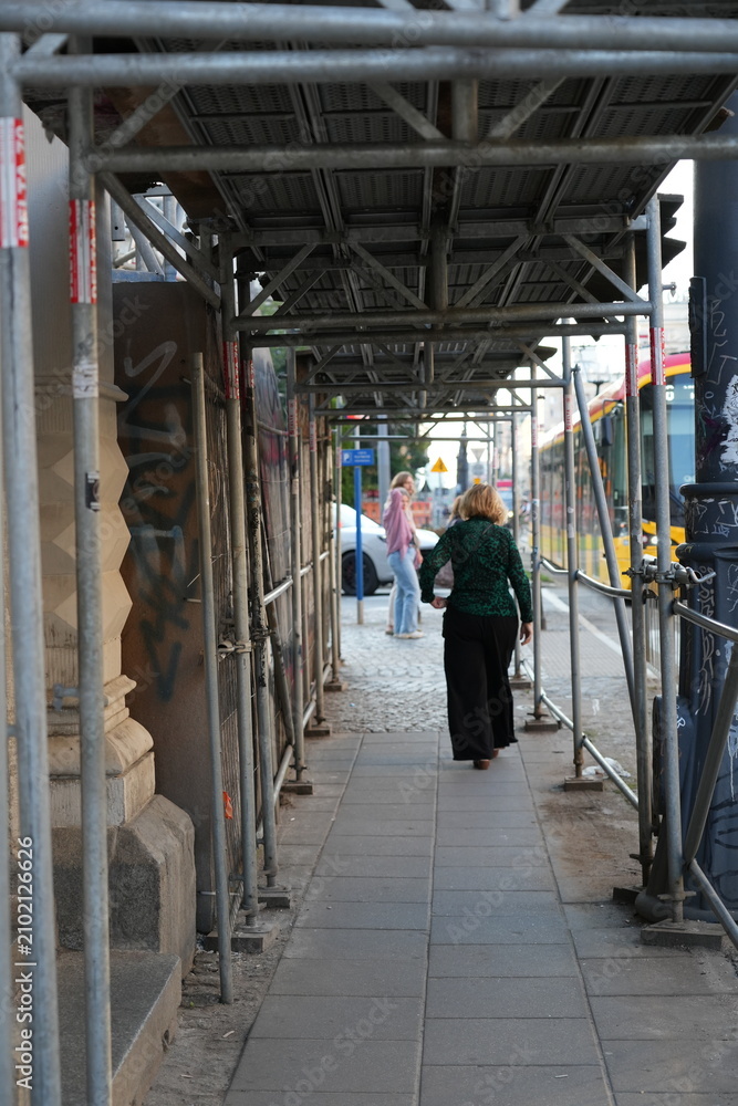 Fototapeta premium Pedestrians walking under metal construction scaffolding on a city sidewalk in Warsaw