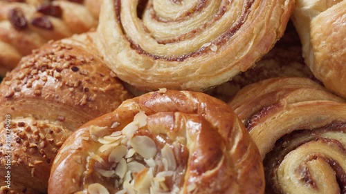 assorted freshly baked sweet pastries rotating on a dark wooden table closeup, food background. Selection of golden brown bakery buns