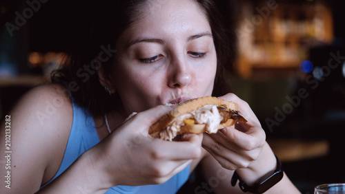 Принти на полотні woman eating sandwich in dark setting with contentment close-up hand bread filling food lifestyle blue brown commercial natural light clean copy space editorial educational visual story web