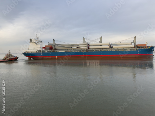 Canvas Print Large cargo ship maneuvering in commercial industrial port, transporting massive wind turbine blades as deck cargo