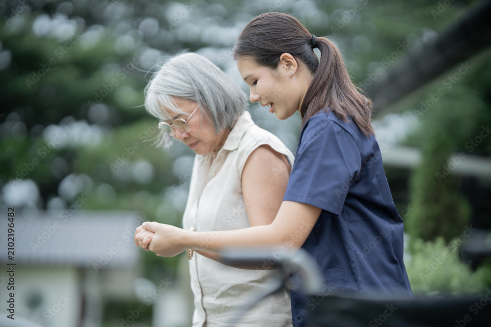 Fototapeta premium Asian caregiver assisting elderly woman in wheelchair, providing compassionate rehabilitation, healthcare, trust, support, dignity, comfort, and happy family connection.