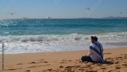 A Jewish person contemplatively observes the Mediterranean waves along the Israeli coast.
