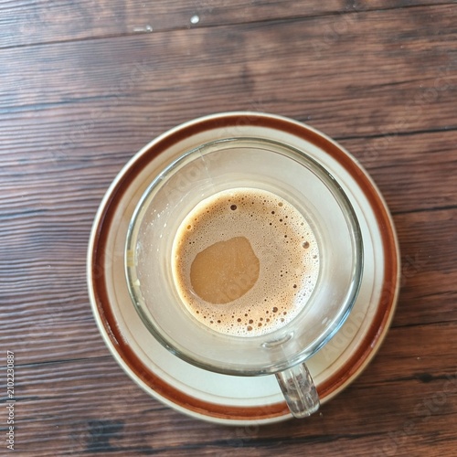 Hot Milk Coffee in Clear Glass Cup on Ceramic Saucer over Wooden Table, Cozy Cafe Beverage Close Up