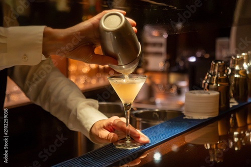 Bartender pouring a cocktail into a martini glass at a bar