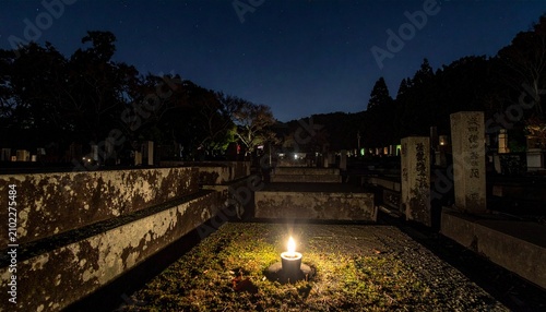 夜中の日本の墓地で1本のろうそくの火でぼんやりてらされている写真