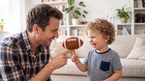 American football father and toddler son balance a soft football toy on one finger for playful indoor family marketing