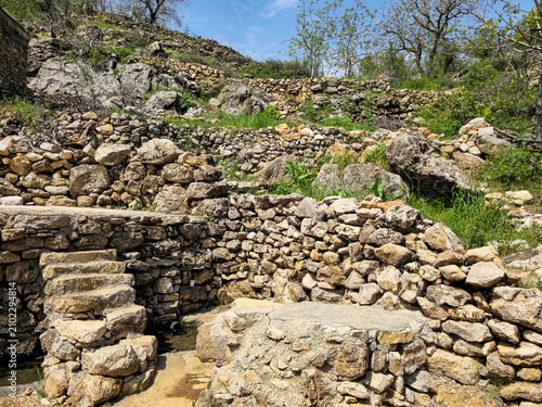 Принти на полотні Terraced stone walls and stairways built into a rocky hillside surround a small natural spring flowing among the stones