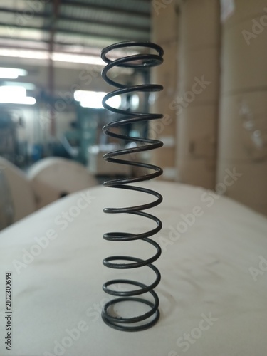 Black metal coil spring standing on white surface in factory setting