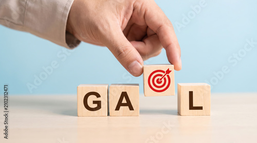 A hand placing a wooden block with a target icon to complete the word goal for business success