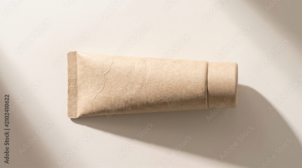 Obraz premium Blank eco-friendly cosmetic squeeze tube mockup made of recycled cardboard paper on beige background with soft natural shadows