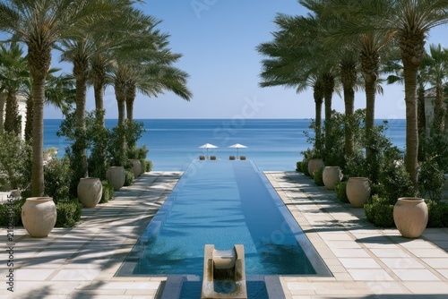 Long infinity pool leads to tranquil ocean vista, framed by palms