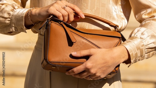 Woman holding stylish tan leather crossbody bag against neutral backdrop