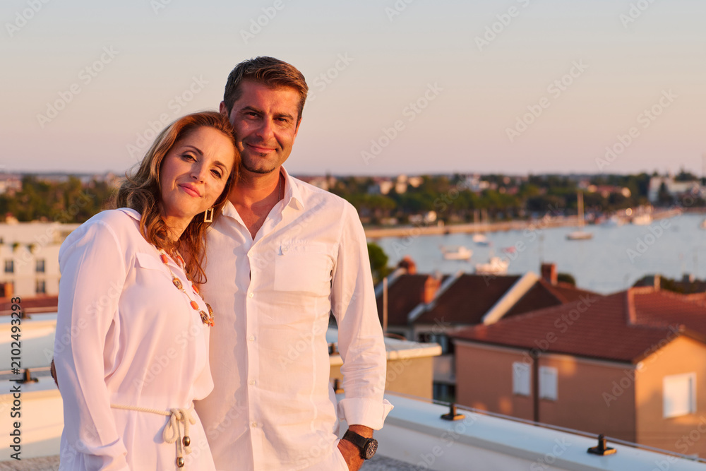 Obraz premium Mature Couple Relaxing on Rooftop Balcony With Sea View at Sunset in Coastal Town