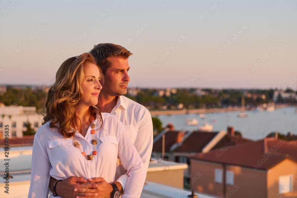 Obraz premium Mature Couple Embracing on Rooftop Balcony With Sea View at Sunset in Umag, Croatia