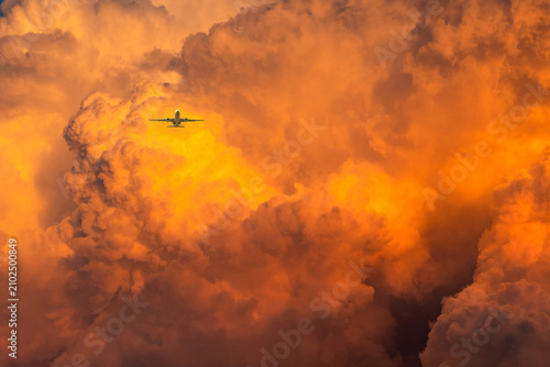 Canvastavla Commercial passenger airplane flying through glowing cumulonimbus clouds at sunset, surrounded by fiery orange storm formations, symbolizing aviation, travel, weather and atmospheric adventure