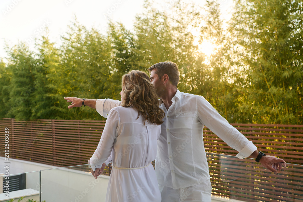 Obraz premium Couple On Home Balcony At Sunset Pointing Over Rooftop Terrace With Relaxed Romantic Vibe