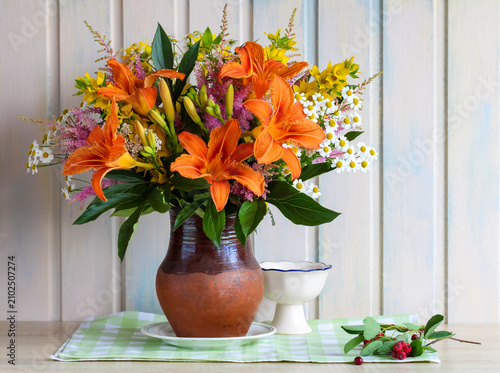 light still life with lilies and daisies on a table in a cottage. garden flowers in a jug by a wooden wall.