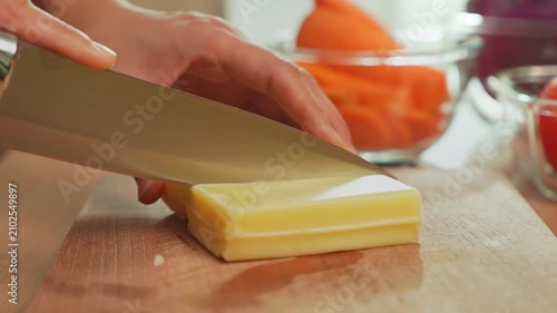 Woman’s hand slicing cheese with kitchen knife on wooden cutting board