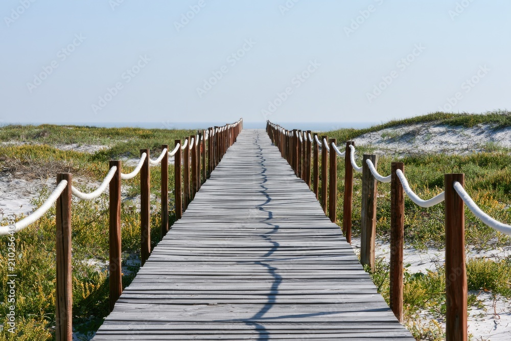 Fototapeta premium Wooden boardwalk leads over sand dunes toward the ocean horizon