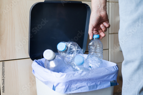 Photos Person placing empty plastic bottle into a kitchen recycling bin, actively separ