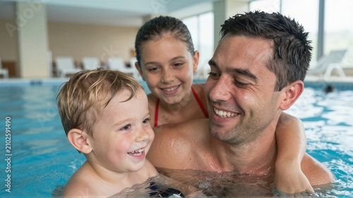Father and children enjoying swim together in indoor pool with bright window light and shallow water play