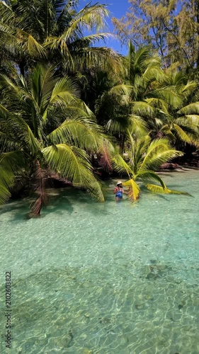 An Asian woman visits the tranquil shores of Koh Kood, Thailand, where clear waters gently lap against sandy beaches. Lush palm trees sway in the warm breeze as nature's beauty unfolds.