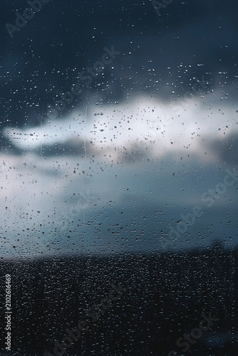 Raindrops dance elegantly on a window while dark clouds loom ominously above the horizon during a stormy evening