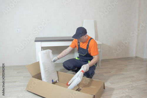 Cuadro en lienzo A middle-aged man in glasses and a special jumpsuit is sitting in front of an open box of furniture in a lighted room
