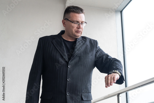 фотографія Businessman in a formal suit walking through a business district while checking his wristwatch
