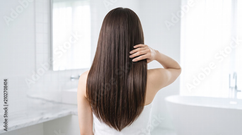 Back view of a woman touching her shiny, wet hair in a modern bathroom
