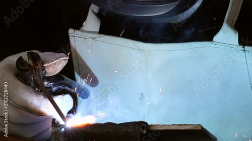 Close up of a man in safety gloves holding electrode holder with flying sparks and smoke