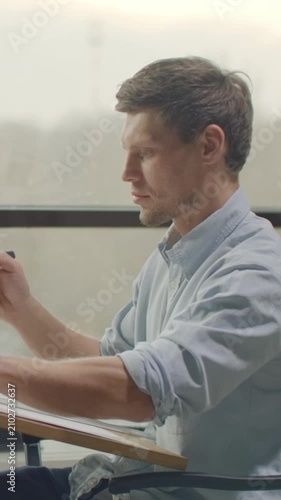 man writing at a desk in a concentrated and focused office or study environment with blue and gray tones and wooden desk and paper materials, side view, business and education context.