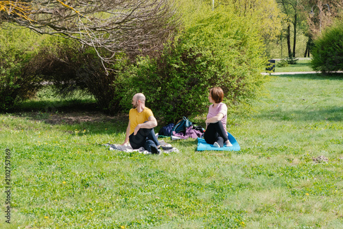 Obraz na płótnie Active middle-aged couple practicing yoga twist pose on grass in public park on