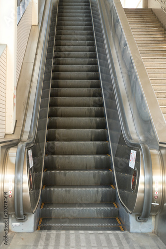 Фотография シンメトリーな構図で捉えた駅の無人エスカレーターの直線美。非常停止ボタンと安全警告ステッカー