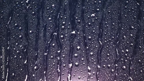 Raindrops cascading down a glass surface with bubbles and streaks of water creating a refreshing aesthetic
