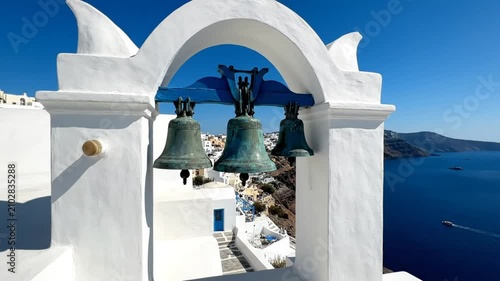 Scenic coastal view through white arch with bronze bells, blue sea and traditional Greek island architecture