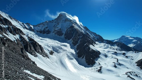 Majestic snow-covered mountain peak with a glacier under a vibrant blue sky on a bright sunny day