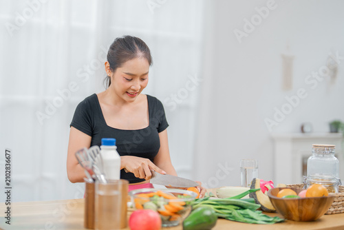 Woman kitchen vegetable cooking cutting home food Asian smiling healthy woman cutting vegetable bright kitchen with fresh ingredient table, relaxed cheerful expression, home meal preparation