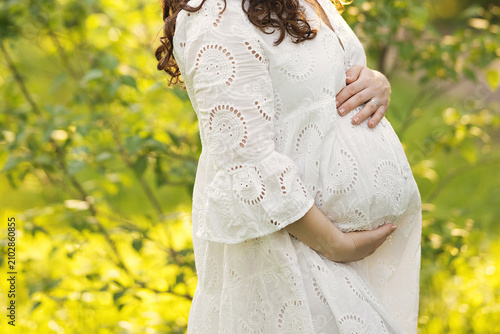 Canvas Print A pregnant woman stands in a sunny garden, gently cradling her belly
