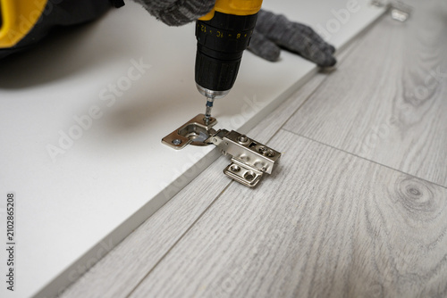 Furniture assembly. Close-up of man installing hidden cabinet hinge using screwdriver. Concept: interior design, real estate development, flat pack furniture assembly