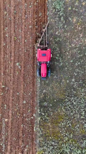 a red tractor plowing a field with a plow, drone view